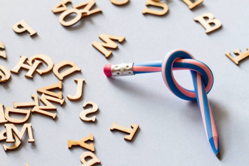 A pencil tied in a knot beside scattered wooden letters